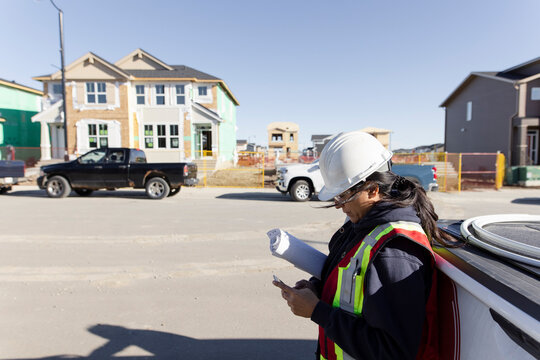 Female Engineer Using Smart Phone At Sunny Housing Development