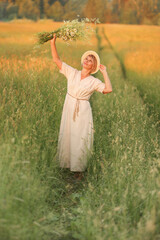 Naklejka na ściany i meble a beautiful woman in a simple linen dress in a field with a bouquet of wildflowers in her hands in the setting sun. Folklore simple style.