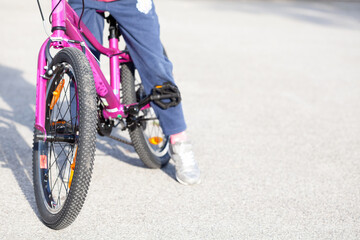 Anonymous young elementary school age child, girl sitting on a bike, legs closeup, front view, copy space background. Kid sitting on a bicycle, means of transport, healthy physical activity concept