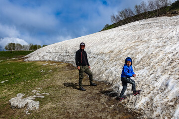 Fototapeta premium A man with a child near a glacier on the Lago-Naki plateau. Snow in Adygea. Russia. 2021.