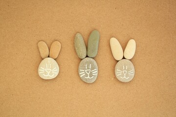 Bunny faces from pebbles on craft paper background. Creative minimalistic easter postcard, banner, poster. Diy save planet, ecological, zero waste, natural stones design concept.  Top view, flatlay. 