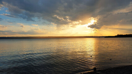 Romantische und Entspannende Landschaft. Sommer Sonnenuntergang am Ammersee. Glühende Sonn spiegelt sich im See, Blauer Himmel voller Wolken und Farben. Feurige orange Farben am Horizont. Bayern.