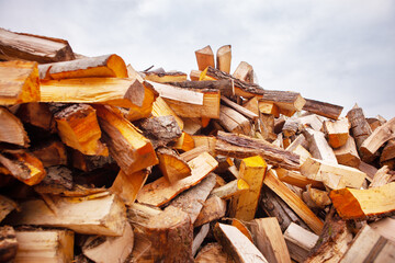 A pile of split firewood for heating a house, in an open space, close-up, against a blue cloudy sky.