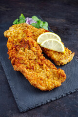 Traditionelles frittiertes Schnitzel mit Zitronenscheiben und Zwiebelringen serviert als close-up auf einem schwarzen Tablett