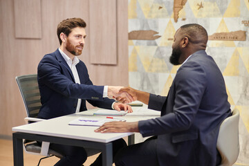 Positive closure of the business meeting. Interracial handshake and positive face expression.