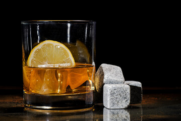 glass of whiskey with ice and lemon. cooling cubes on a dark background.