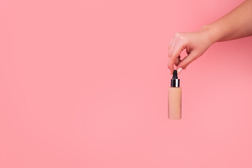 Foundation with a female hand on a pink background. BB cream for professional make-up, eyedropper for applying to the face. Cosmetic female accessory, liquid fluid. Mock up concept