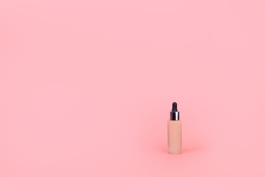 Foundation with a female hand on a pink background. BB cream for professional make-up, eyedropper for applying to the face. Cosmetic female accessory, liquid fluid. Mock up concept