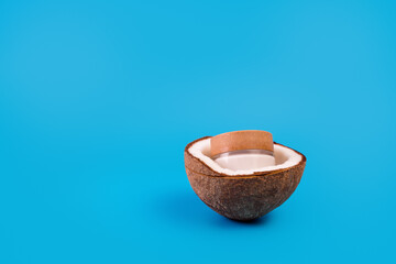 Coconut cream in glass jar with fresh coconut split in half on isolated blue background. Cosmetic moisturizer with retinol in a glass container. Natural beauty organic moisturizing cream.