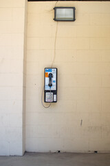 Old Coin-Operated Public Telephone Booth In Front Of Yellow Brick Wall