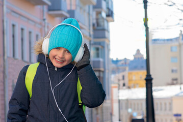 happy schoolboy goes to school and listens to his favorite music in headphones. Happy childhood.Happy little girl listen to music. Small child with happy smile. in Spring clothes, warm hat and jacket.