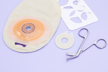 A colostomy bag, a stencil with sizes of different diameters and medical scissors lie on a lilac.