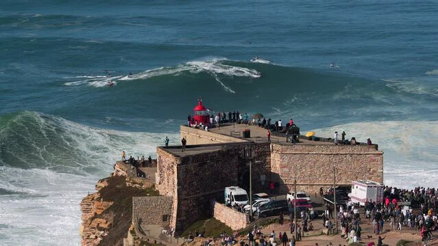 Surfer riding giant wave near historical landmark Fort of Sao Miguel Arcanjo Lighthouse in Nazare, Portugal. Nazare is famously known to surfers for having the largest waves in the world.	