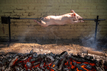 A young suckling pig on a skewer. Whole roasted pig on a rotating steel spit with fire and smoke....