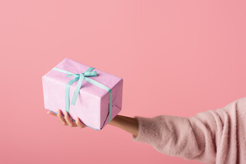 cropped view of young woman holding wrapped gift box isolated on pink.