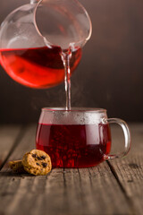 A cup of freshly puring red tea, warm soft light, dark backround on wooden table