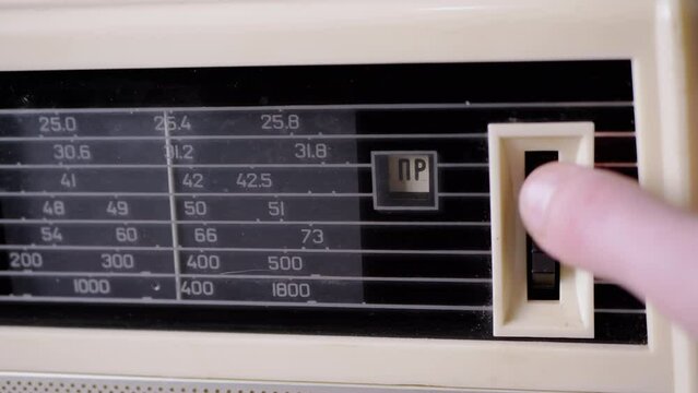 A Female Fingers Tuning the Frequency on an Old Vintage Analog Receiver. Search for a music radio station on a dial scale on panel of a short-wave portable FM radio, player, tape recorder 80s, 90s.