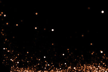 Blurred sparkles of gold color falling against black background.