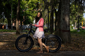 Young Latin American woman (33) goes for a walk in spring in the park with her electric bicycle,...