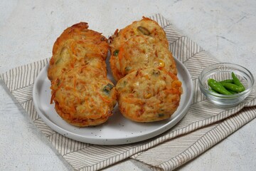 Bakwan Pontianak or vegetable fritters is an Indonesian traditional snack made from wheat flour mixed with vegetables and topping with dried shrimps. Served with sour and spicy sauce in white plate.