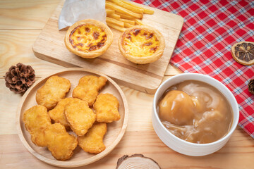Egg tart or Portuguese egg tart and Chicken nuggets in wooden plate on wooden background, Homemade egg tart and french fries dessert on wooden table.