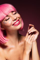 joyful woman with pink hair and shiny stones on face smiling on dark purple.