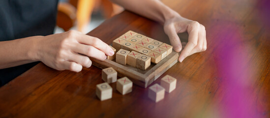 Female hand play tic-tac-toe wood board game XO on a wooden surface. Toys with wooden boxes.