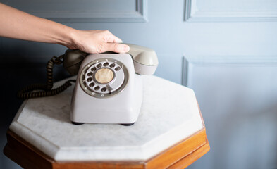 Female hand holds The old grey telephone set of the 70s of the 20th century stands on the classic wooden table indoor room.