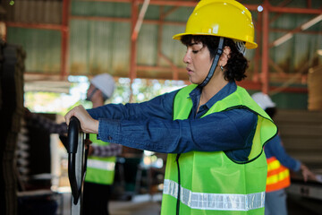 Female warehouse worker in safety uniform and hard hat works by hydraulic jack lift piles of cardboard for shipping and logistic transport at manufacture factory, supply packaging stocks industrial.