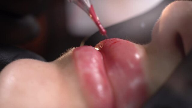 Microblading lip tattoo with a special coloring red pigment that corrects lip color, make-up in a cosmetology clinic. Permanent lip makeup procedure with application of pigmented