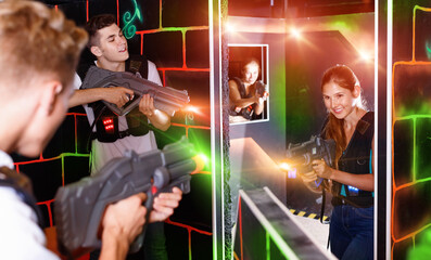 Laser tag players positive guys and girls playing in teams in dark laser tag room
