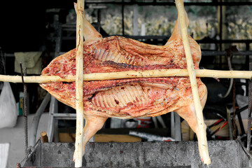 barbecued suckling pig on a grill with wooden coal. Whole roasted piglet body turning on grill.