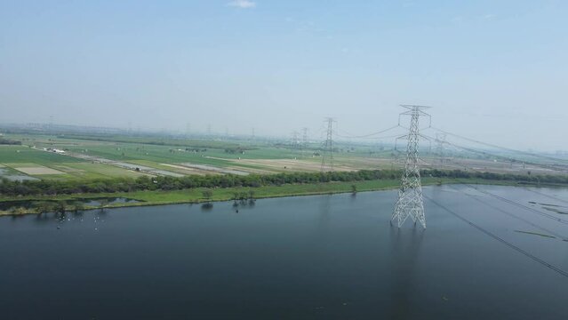 Aerial Drone shot of over agricultural land and electric high voltage pylon against beautiful sky in ocean.