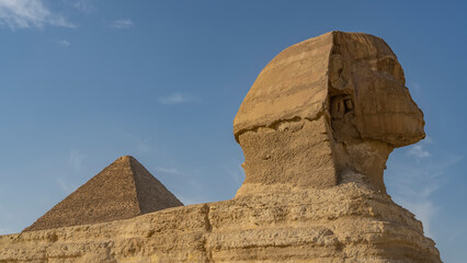 Sculpture of the Great Sphinx. Close-up. Profile view. The texture of the weathered surface of the stone statue is visible. The top of the pyramid against the blue sky. Egypt