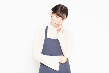 白い背景の前に立って悩んでいるエプロンをつ