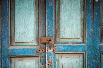 Blue wooden doors with rough texture locked by rusty key lock.