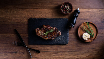 Sliced striploin steak, grillid with 4seasons pepper garlic rosemary, on stone plate dark and wooden background , knife and fork black, top view