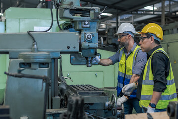 Engineer and assistance in safety uniforms working with heavy machine in machinary factory