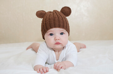 Portrait of a cute newborn baby in a brown knitted hat with ears lying on his stomach on a bed with ears close-up, teddy bear