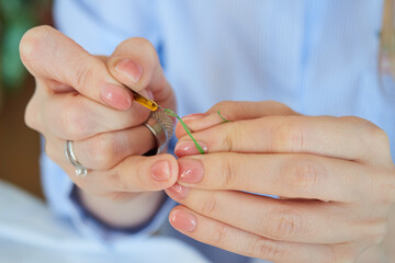 Close-up of female hands inserting a green thread into a needle