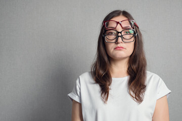 woman with a sad face in three glasses stands against the background of a gray wall, copy space