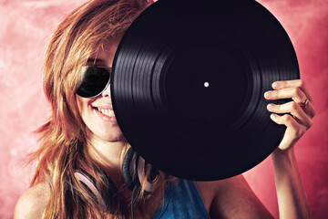 Golden Oldies are still the best. Fun portrait of a young woman holding a vinyl record up to her...