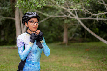 Latin young woman on a bicycle practicing cycling in the forest. Helmet placement, safety.