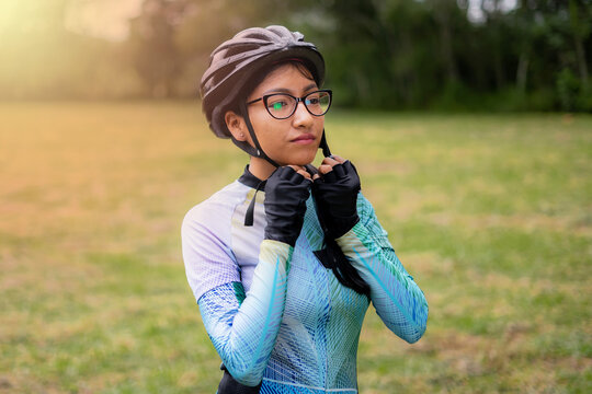 Latin young woman on a bicycle practicing cycling in the forest. Helmet placement, safety.