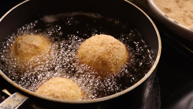 Three Italian arancini rice balls deep frying in hot boiling oil.