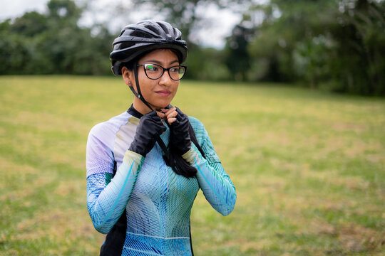 Latin young woman on a bicycle practicing cycling in the forest. Helmet placement, safety.