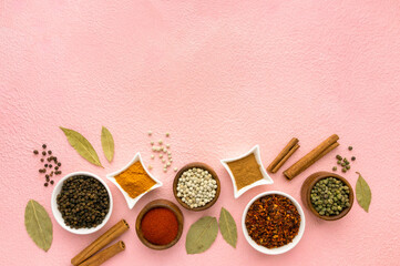 Spices and seasonings in small bowls on pink background, space for text