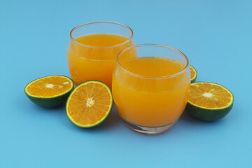 Two glasses of fresh orange juice and green orange fruits slices on blue background	