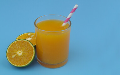 Orange juice with drink straw and orange fruit slices on blue background, copy space for text