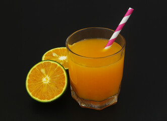 Orange juice with drink straw and orange fruit slices on black background